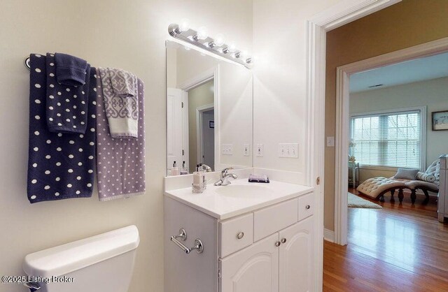 bathroom with toilet, vanity, wood finished floors, and baseboards