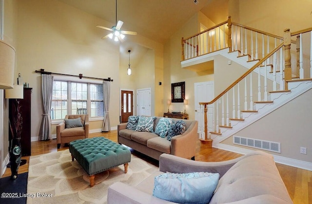 living area with wood finished floors, visible vents, baseboards, high vaulted ceiling, and ceiling fan