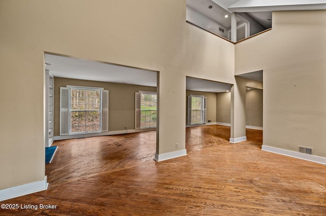 unfurnished living room featuring a high ceiling, wood finished floors, baseboards, and visible vents