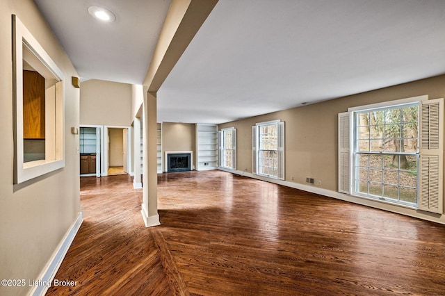 unfurnished living room with a fireplace, dark wood-type flooring, baseboards, and built in features