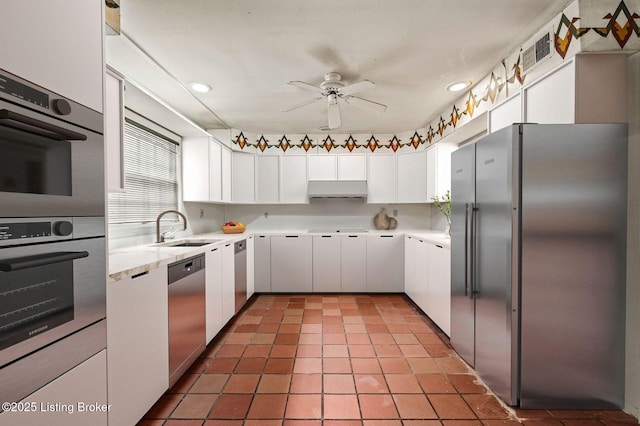 kitchen with a ceiling fan, white cabinets, under cabinet range hood, a sink, and stainless steel appliances
