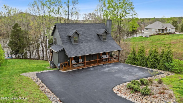 view of front facade featuring a front yard, covered porch, a chimney, driveway, and roof with shingles