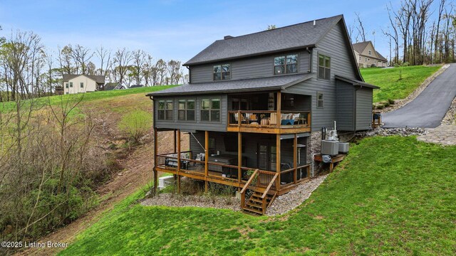 back of house featuring a yard, a wooden deck, a sunroom, and roof with shingles
