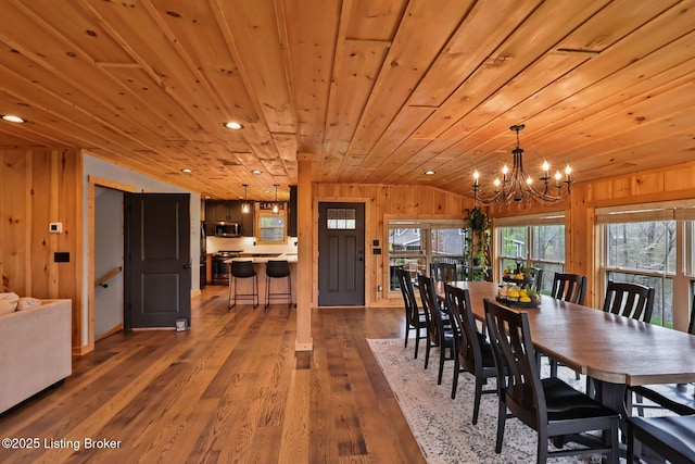 dining area with wooden walls, an inviting chandelier, wood finished floors, and lofted ceiling