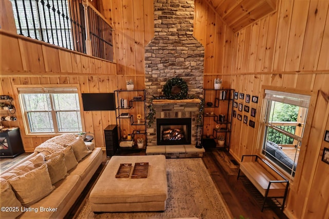 living area with wood walls, wood-type flooring, high vaulted ceiling, and a stone fireplace