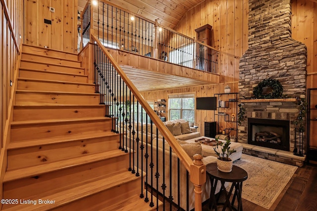 stairs with high vaulted ceiling, a stone fireplace, wood ceiling, wood finished floors, and wooden walls