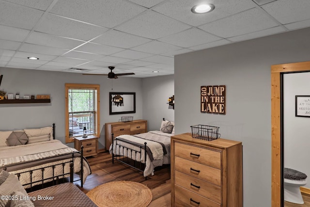 bedroom with ceiling fan, a drop ceiling, and wood finished floors