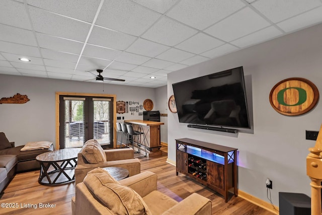 living area with baseboards, french doors, ceiling fan, a drop ceiling, and wood finished floors