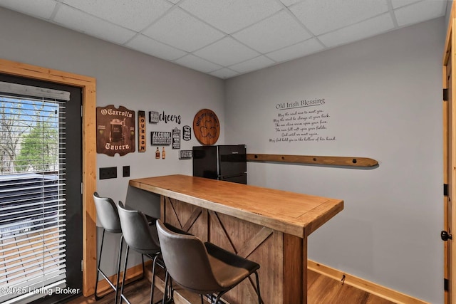 bar featuring a paneled ceiling, wood finished floors, freestanding refrigerator, and baseboards
