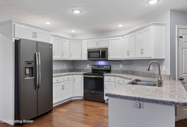 kitchen with a peninsula, a sink, white cabinets, and stainless steel appliances