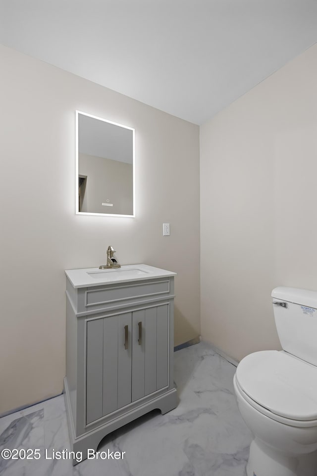 half bathroom with toilet, marble finish floor, baseboards, and vanity