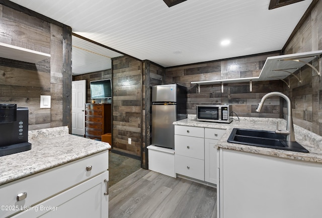 kitchen featuring open shelves, a sink, light wood-style floors, wooden walls, and stainless steel appliances