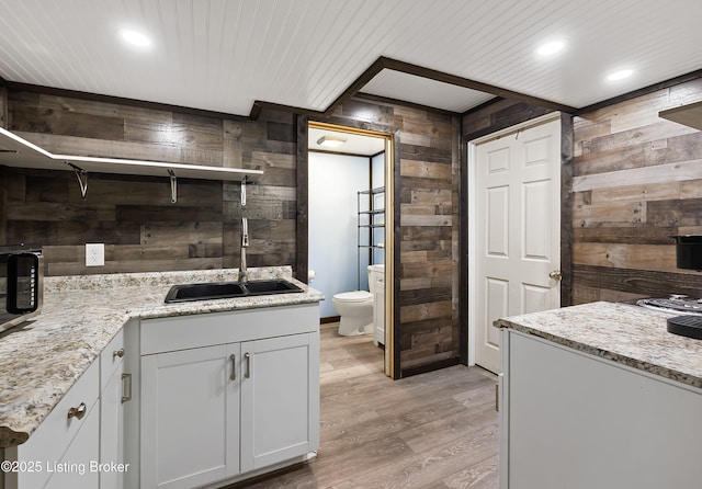 kitchen with light stone counters, wooden walls, open shelves, light wood finished floors, and a sink