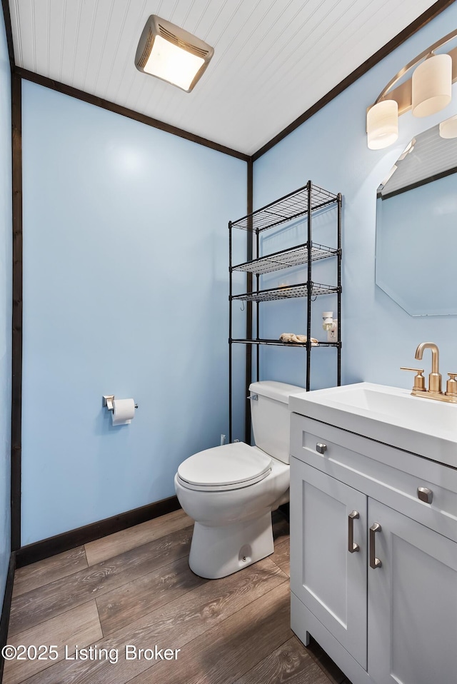 bathroom featuring toilet, vanity, wood finished floors, and baseboards