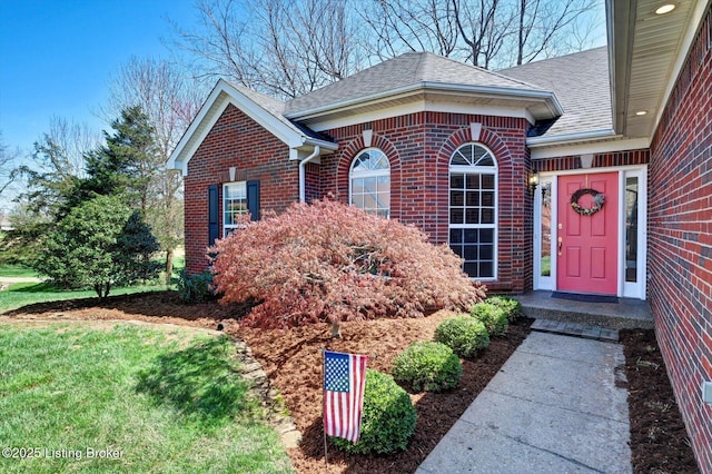 view of exterior entry featuring roof with shingles and brick siding