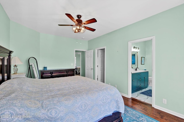 bedroom featuring dark wood-type flooring, ensuite bath, a ceiling fan, a sink, and baseboards