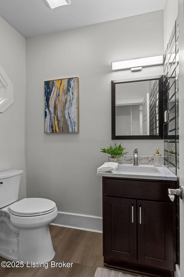 half bath featuring vanity, baseboards, toilet, and wood finished floors