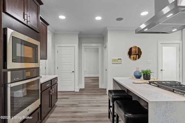 kitchen with light wood-style floors, wall chimney exhaust hood, dark brown cabinetry, ornamental molding, and built in microwave