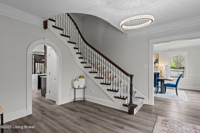 foyer entrance featuring crown molding, arched walkways, wood finished floors, and stairs