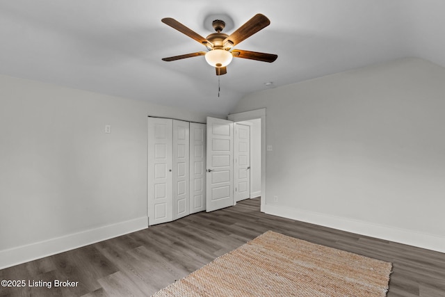 unfurnished bedroom with a closet, baseboards, wood finished floors, and lofted ceiling