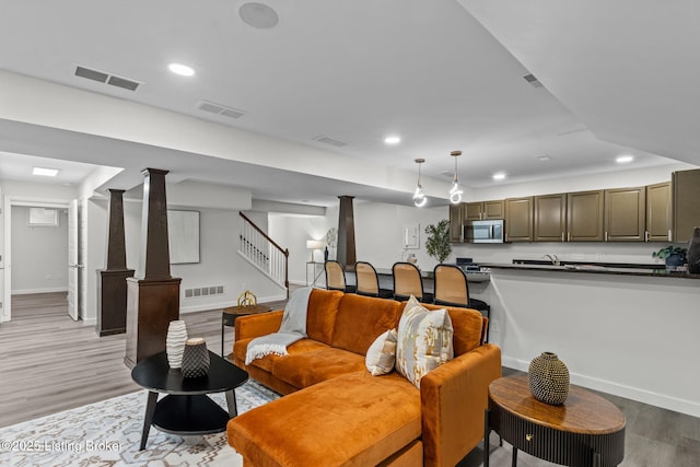 living room with light wood-style floors, stairs, visible vents, and baseboards