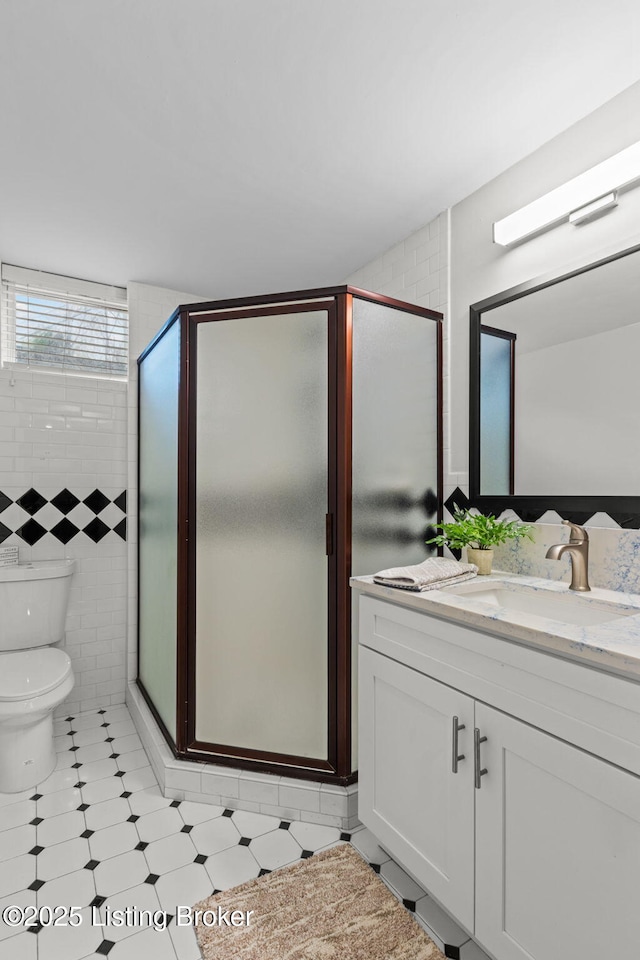 full bath featuring a shower stall, tile walls, vanity, and toilet