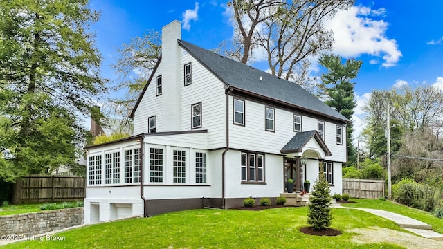 view of front of home with a sunroom, a garage, a chimney, fence, and a front lawn