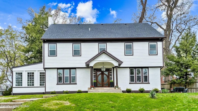 colonial home with a front lawn, fence, and a shingled roof