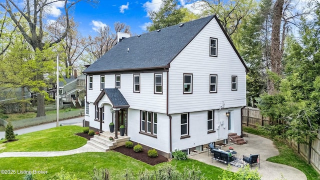 exterior space with a shingled roof, a chimney, a fenced backyard, a patio, and a front lawn