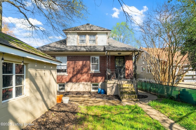 rear view of house featuring brick siding, fence, and roof with shingles