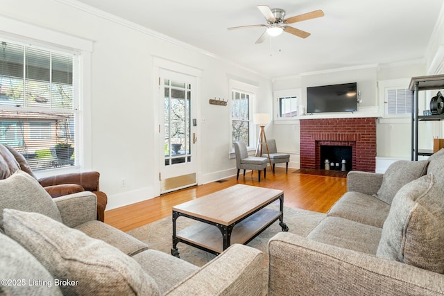living room with ceiling fan, ornamental molding, wood finished floors, a brick fireplace, and baseboards