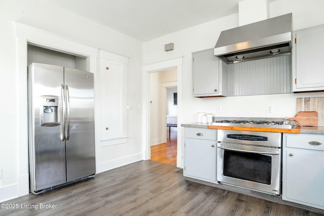 kitchen with dark wood-type flooring, light countertops, wall chimney exhaust hood, and stainless steel appliances