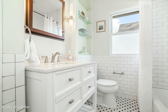 full bathroom featuring vanity, tile patterned flooring, a wainscoted wall, toilet, and tile walls