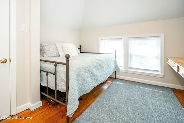 bedroom featuring baseboards, wood finished floors, and lofted ceiling