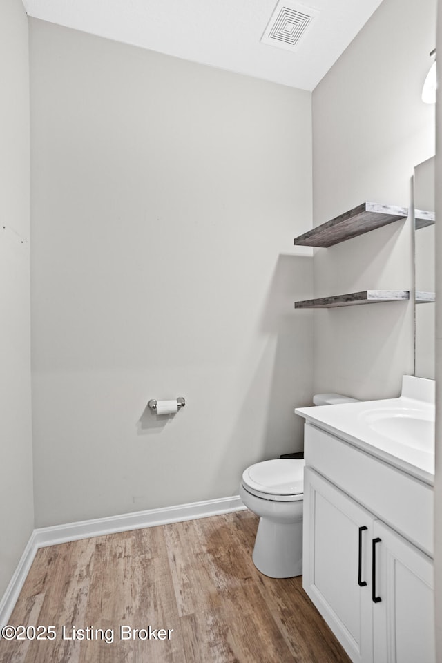 half bathroom featuring visible vents, toilet, vanity, and wood finished floors