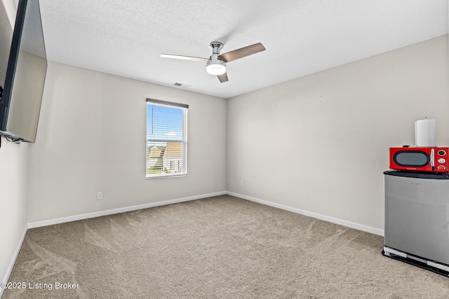 unfurnished room featuring carpet, a textured ceiling, a ceiling fan, visible vents, and baseboards