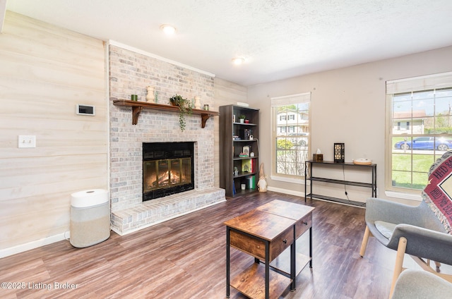 living area with a fireplace, baseboards, wood finished floors, and a textured ceiling