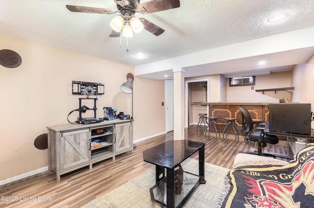 living area featuring a textured ceiling, wood finished floors, bar area, and baseboards