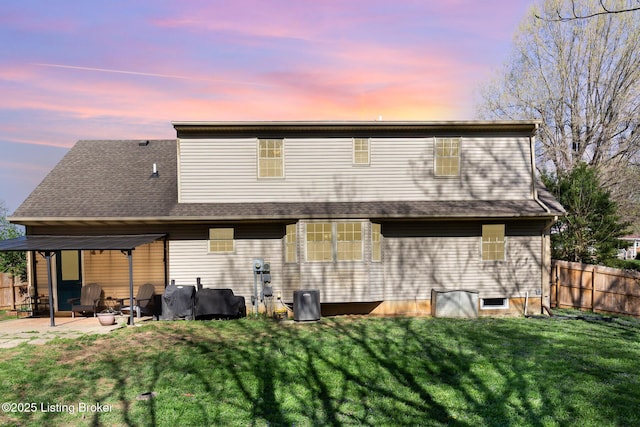 back of house at dusk with a patio area, fence, and a lawn