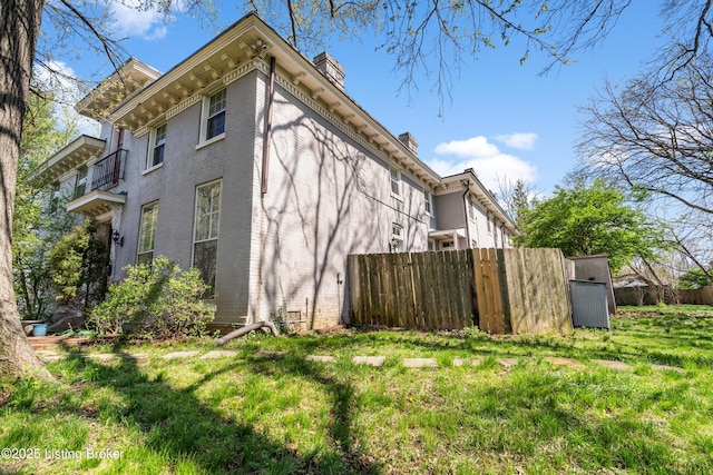 view of side of home with a chimney, fence, and brick siding