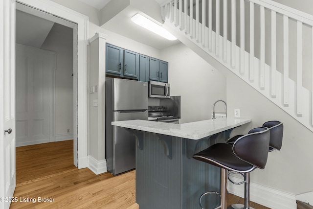 kitchen with light wood-type flooring, a peninsula, blue cabinetry, a kitchen bar, and stainless steel appliances