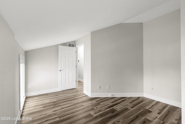 spare room with visible vents, baseboards, vaulted ceiling, and wood finished floors