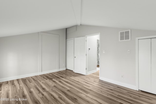 interior space with visible vents, baseboards, wood finished floors, and lofted ceiling