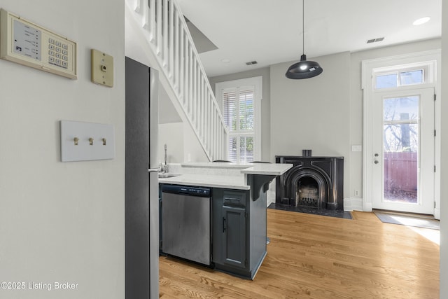kitchen featuring stainless steel dishwasher, a peninsula, visible vents, light countertops, and light wood finished floors