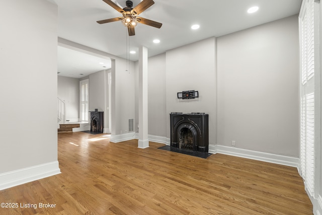 unfurnished living room featuring baseboards, recessed lighting, a wood stove, ceiling fan, and light wood finished floors