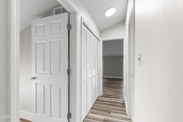 hall featuring wood finished floors, visible vents, baseboards, and vaulted ceiling