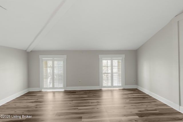 unfurnished room with wood finished floors, baseboards, vaulted ceiling, and plenty of natural light