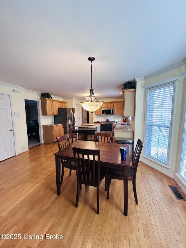 dining space featuring visible vents, light wood finished floors, a wealth of natural light, and ornamental molding