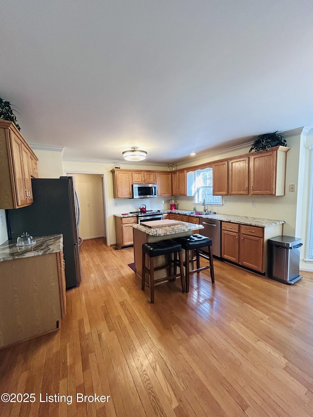 kitchen with stainless steel appliances, a sink, light wood-type flooring, a kitchen island, and ornamental molding