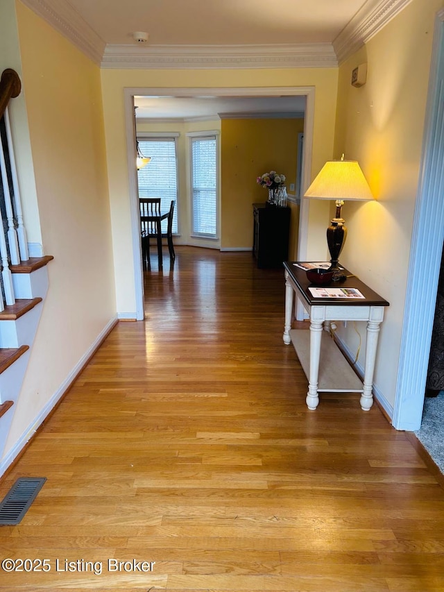 hallway with baseboards, ornamental molding, visible vents, and light wood-type flooring